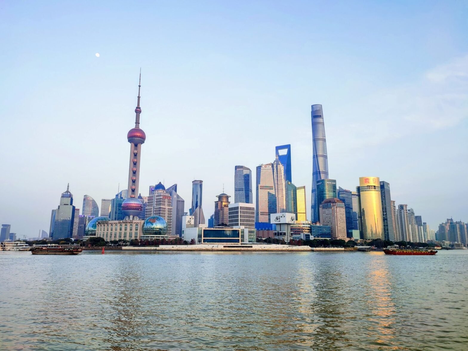 Photograph showcasing Shanghai skyline along Huangpu River, with iconic the Oriental Pearl Tower, Shanghai Tower, and Shanghai World Financial Center.