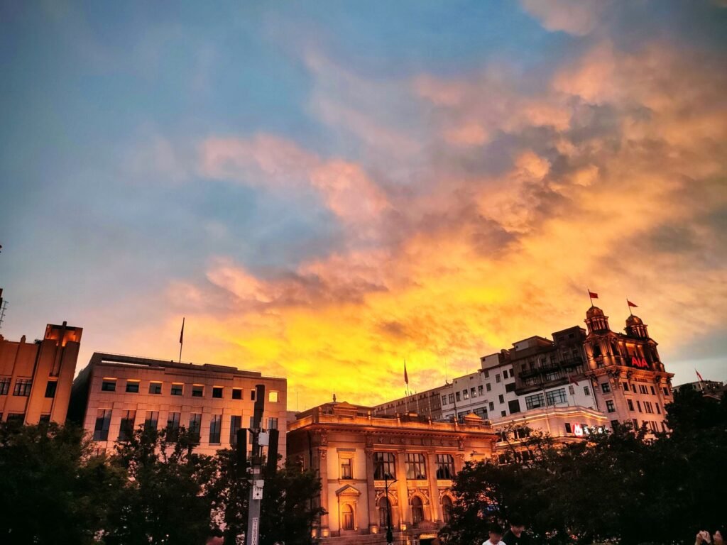 Photograph of an Shanghai skyline beneath vivid orange, pink, and blue sunset clouds.